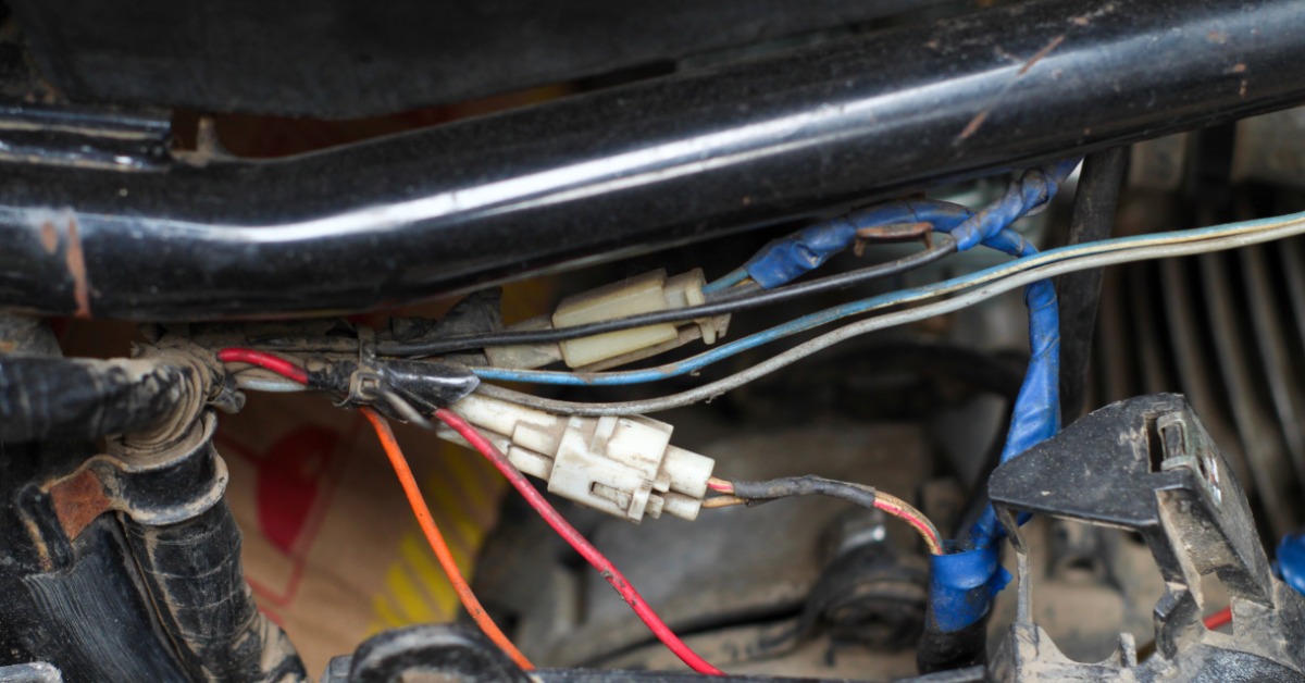 Wires running along a metal pipe in a vehicle in a brightly lit space. Plastic connectors attach wires together.