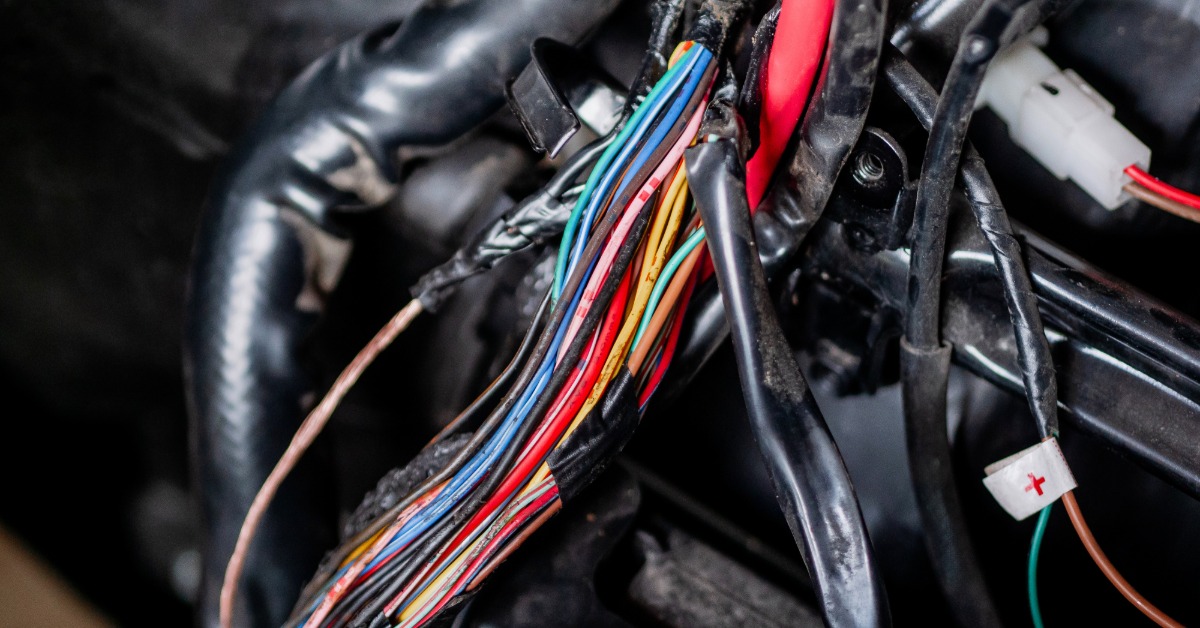 A bundle of multi-colored wires running out of a car. Electrical tape covers many of the wires and connectors.