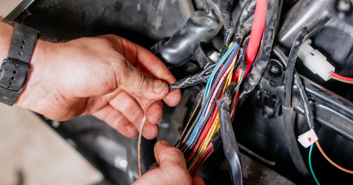A mechanic wearing a black watch organizing many colorful wires extending from a disassembled car dashboard.