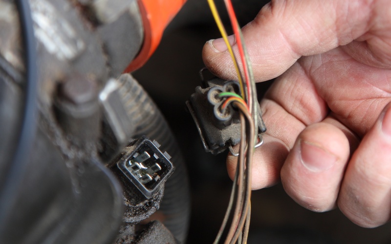 A person disconnecting a four-pin automotive connector attached to green, yellow, red, white, and gray wires.