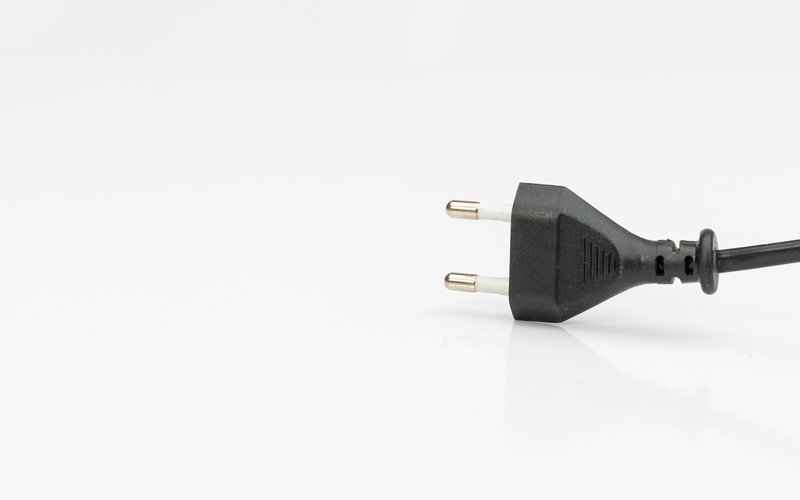 A two-pin connector with a thin black cord. The connector is on a clean, white surface in a brightly lit room.