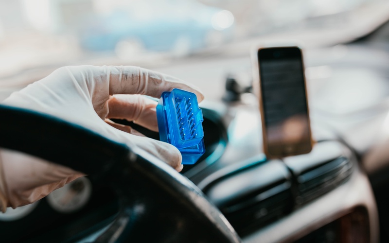 A person wearing a white glove holding a blue automotive connector in front of a car’s interior dashboard.