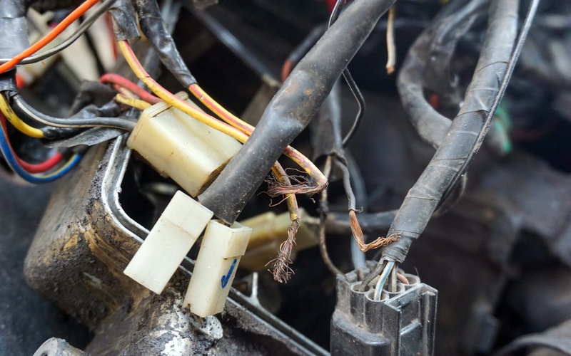 A bundle of automotive connectors surrounded by dirty metal. The connector cables are covered in electrical tape.