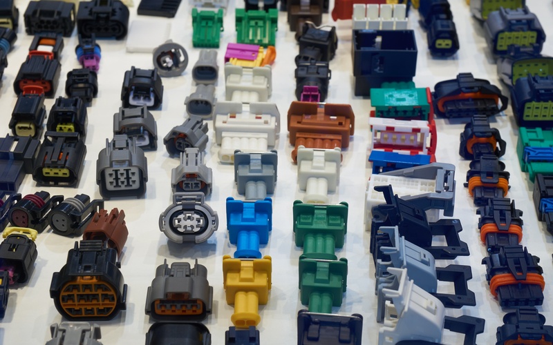 An overhead view of automotive electrical connectors in different colors lined up on a plain white surface.